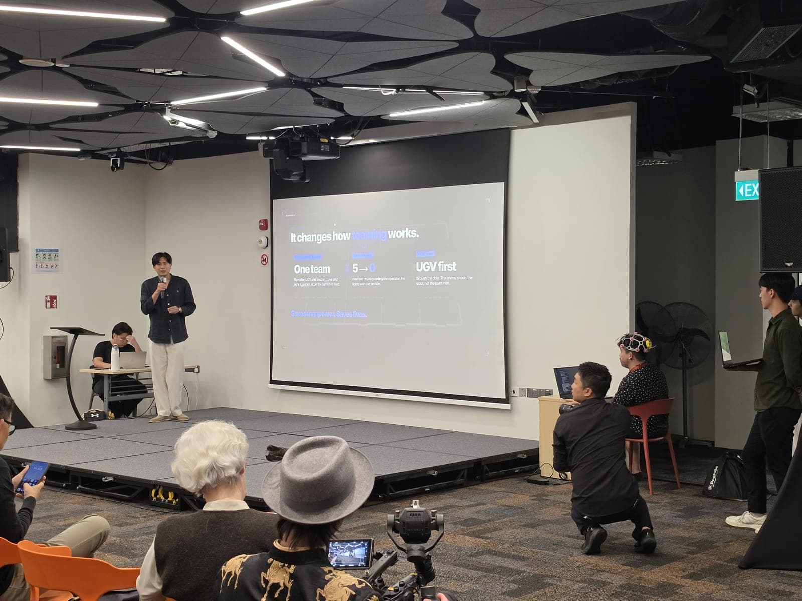 Pitching NeuroMech on stage, with the operator wearing the headset live beside the screen